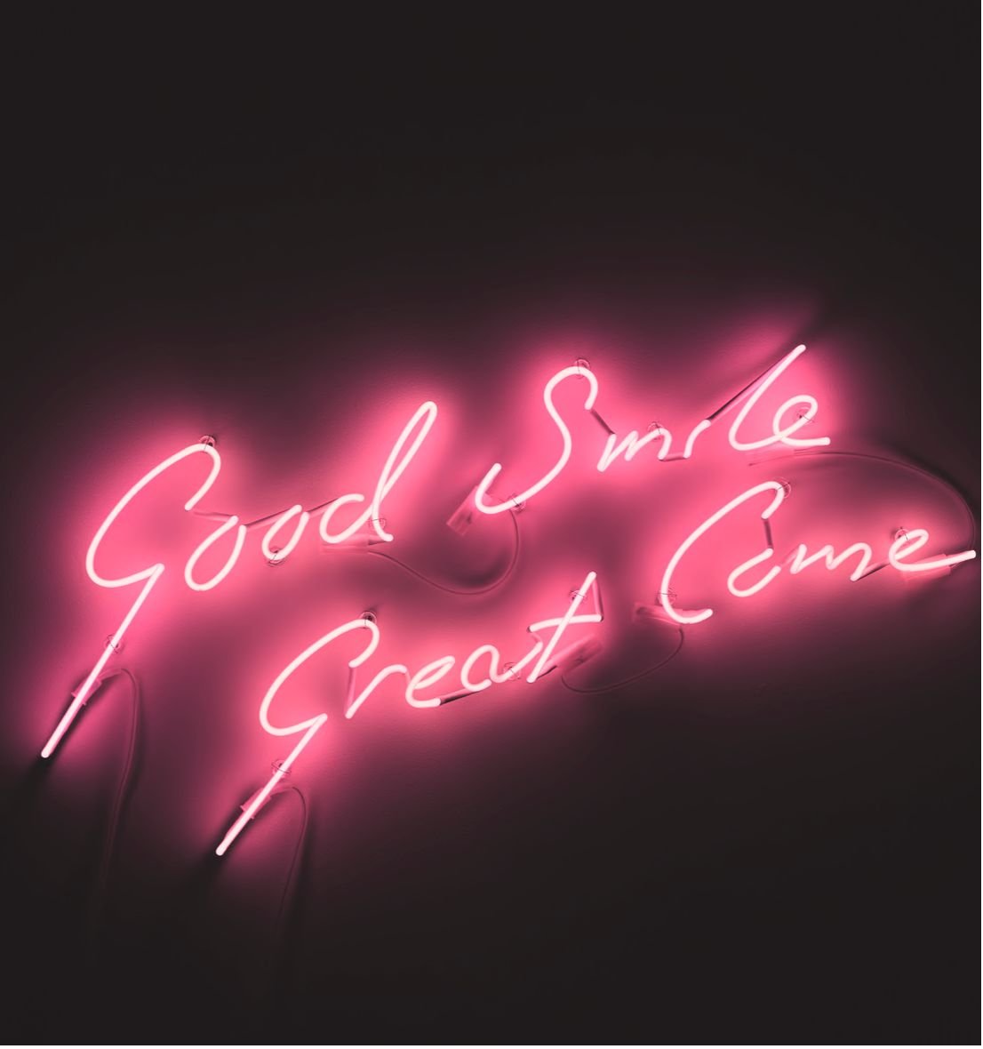 Good Smile Great Come, handwritten words in pink neon on a dark background.